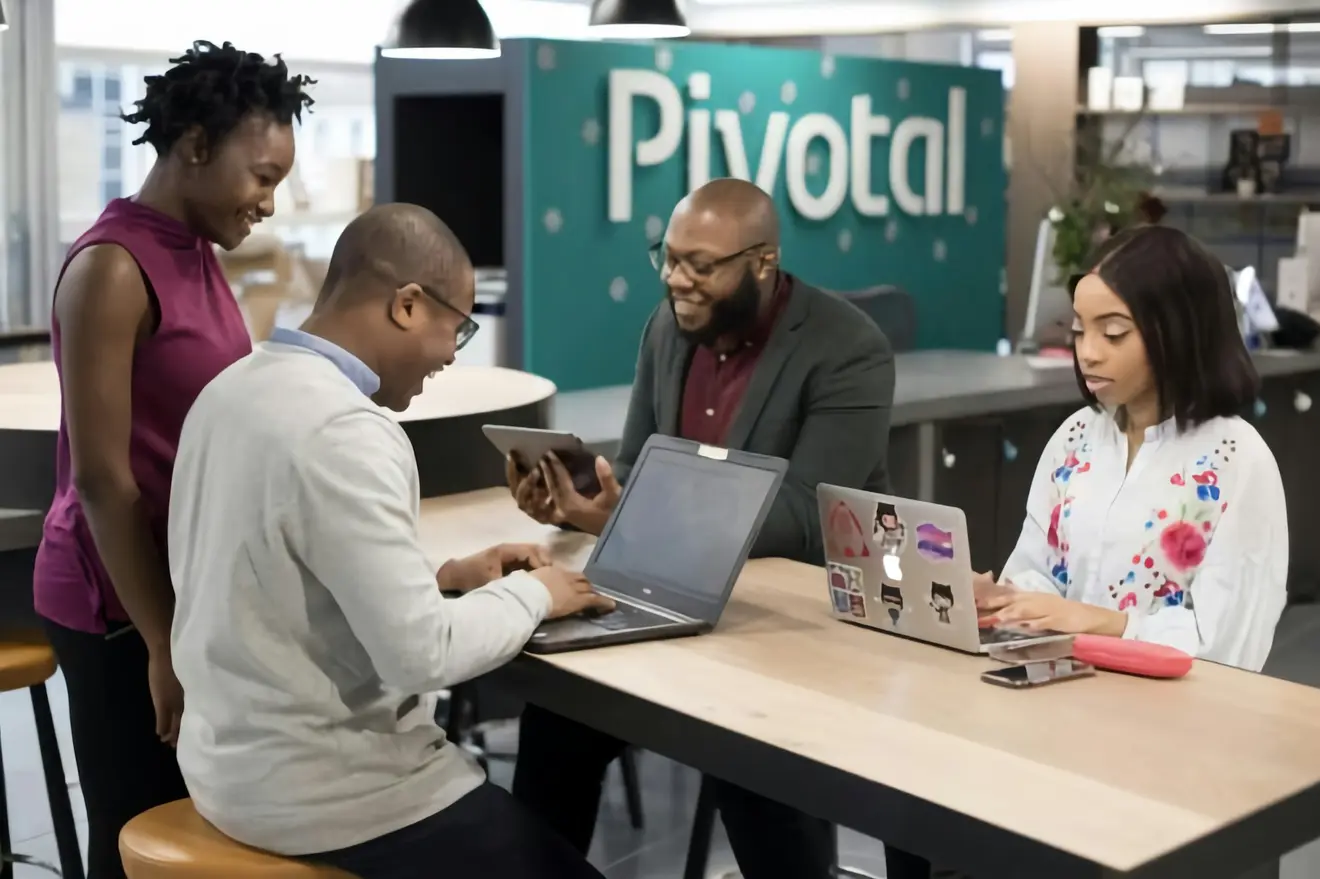 Four people gathered around a table using laptops and a tablet