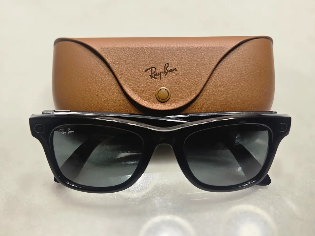 First-generation Ray-Ban Meta glasses beside their brown charging case