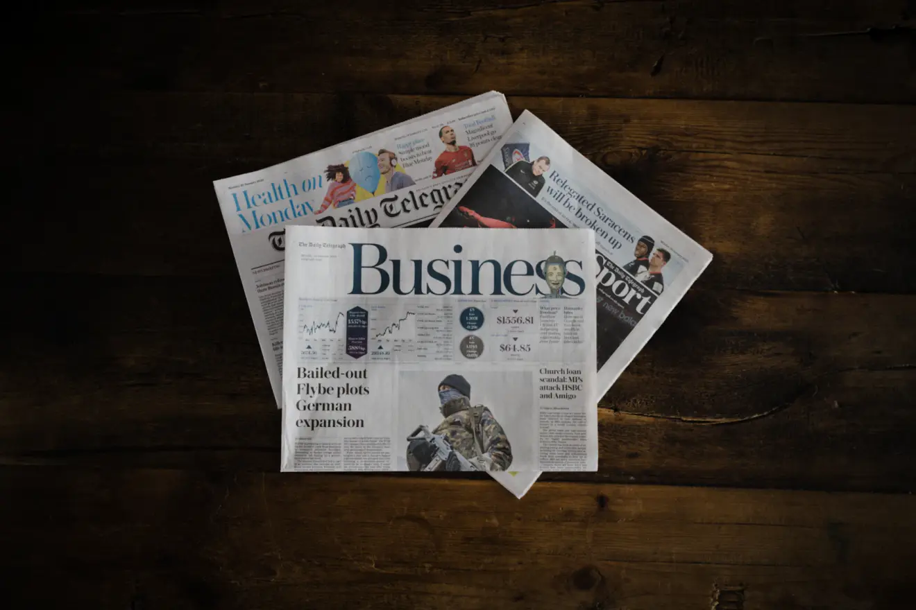 Several folded newspaper sections spread across a wooden table.