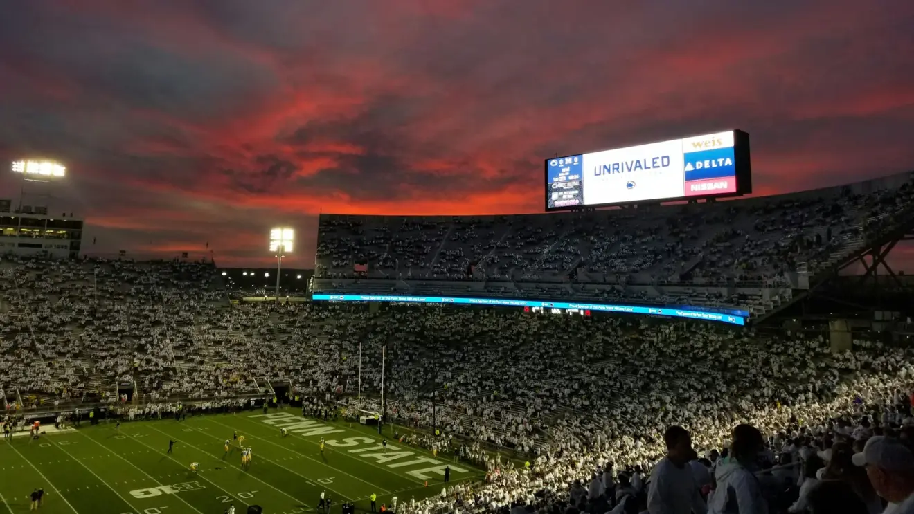 Penn State's Beaver Stadium beneath a red sunset, with fans in the stands and the end zone visible