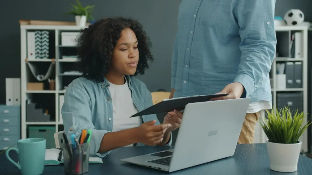 Two colleagues reviewing a document together beside a laptop