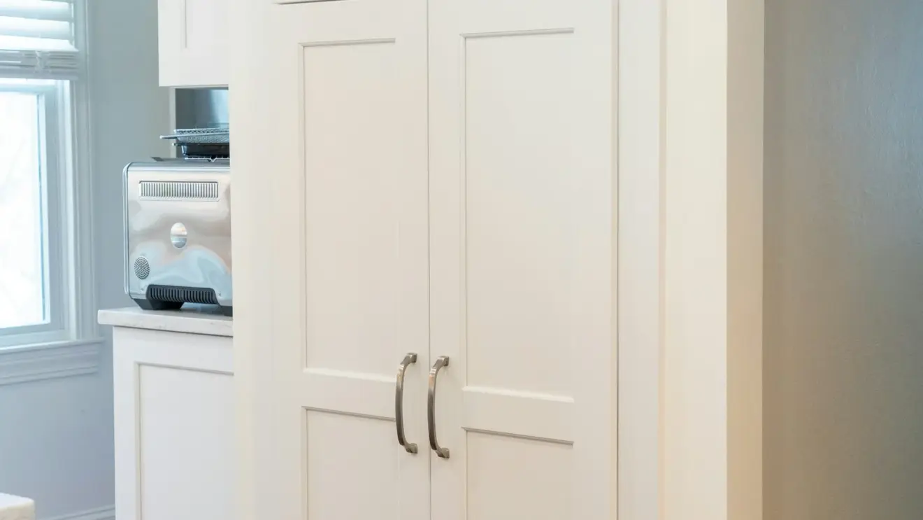 White pantry cabinet doors with silver handles beside a kitchen window