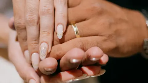 Two hands resting together with wedding rings visible