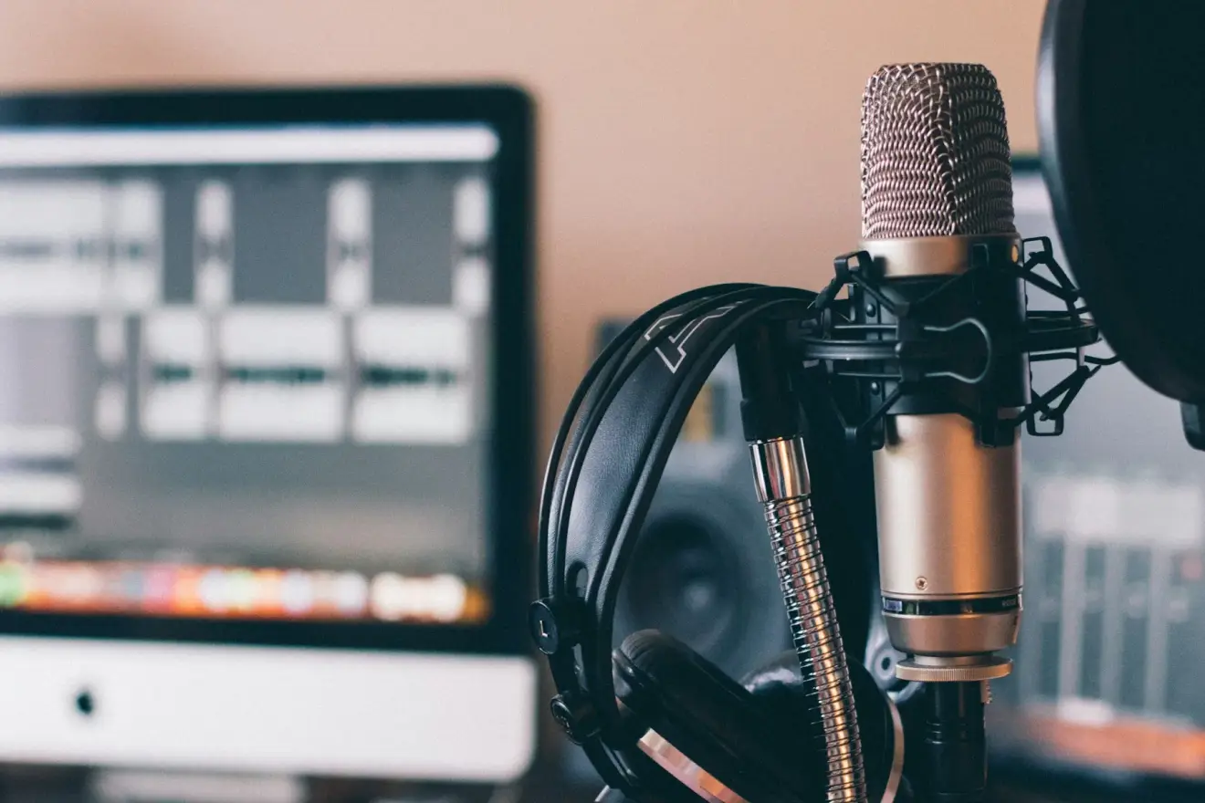 A studio microphone and headphones beside a computer used for audio recording.