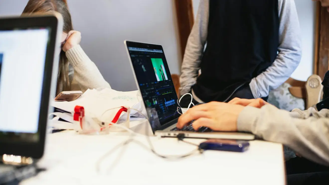 People working together at a table with a laptop open to a video-editing project.