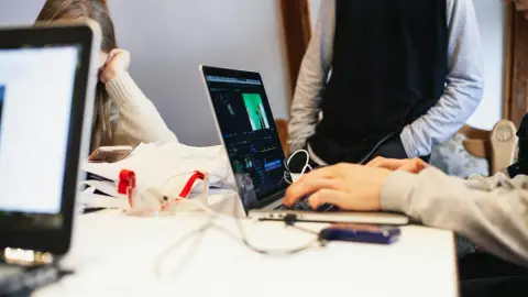 People working together at a table with a laptop open to a video-editing project.