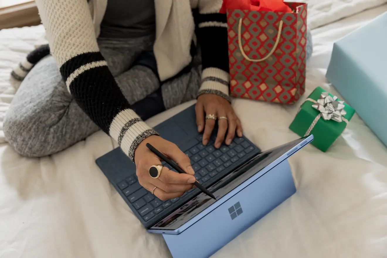 A shopper using a laptop and stylus beside wrapped gifts