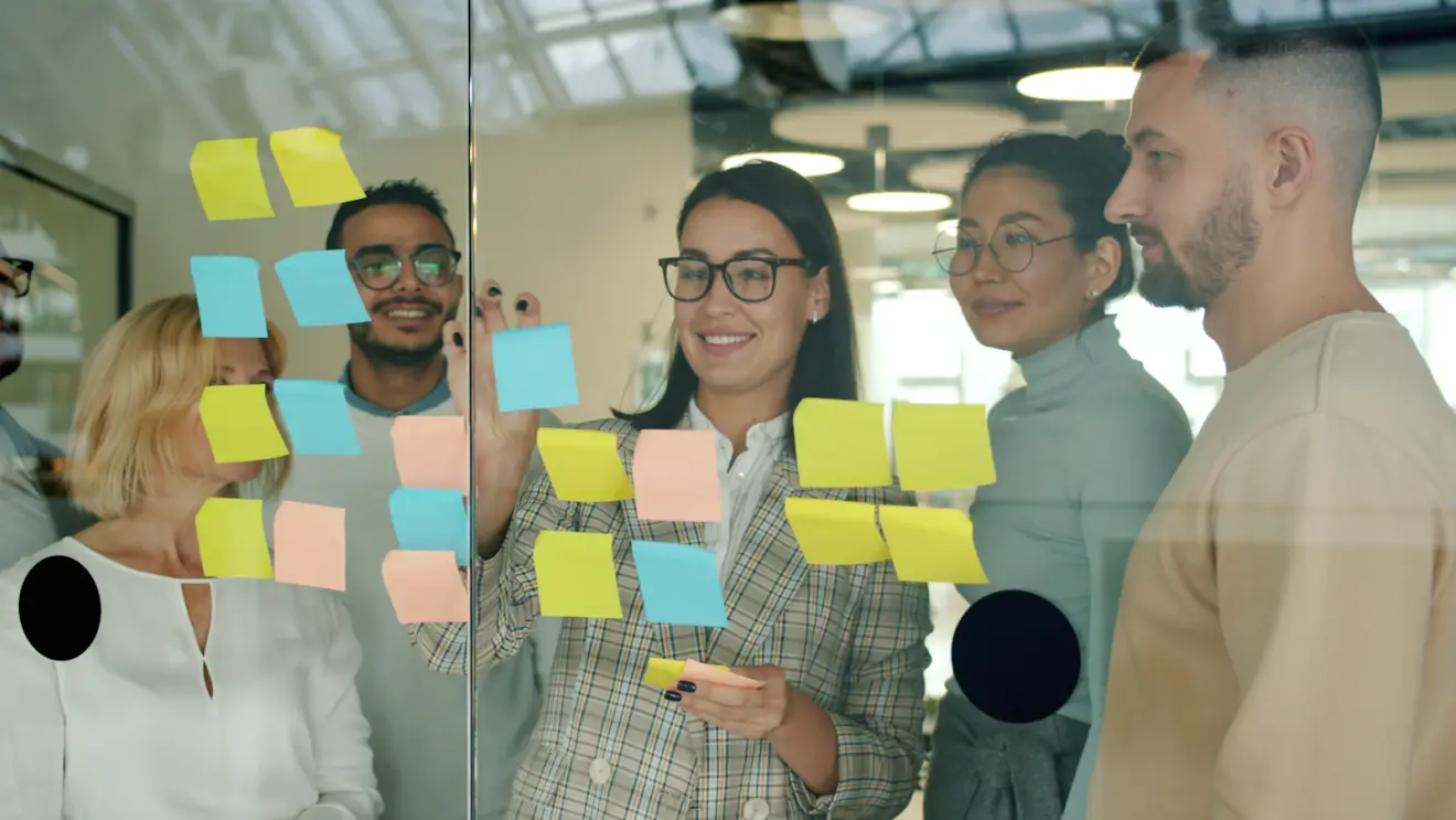 Colleagues discussing colored notes on a shared glass board