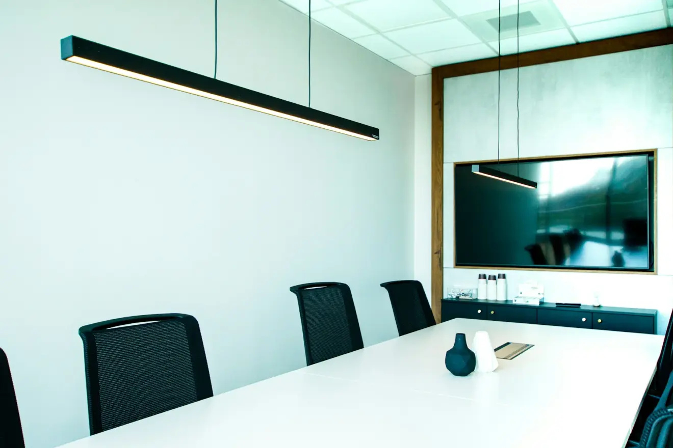 A modern meeting room with a white table, black chairs, and pendant lighting